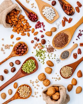 Various legumes and different kinds of nuts in spoons. Walnuts kernels ,hazelnuts, almond ,brown pinto ,soy beans ,flax seeds ,chia ,red kidney beans and pecan set up on white wooden table.