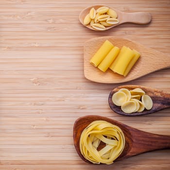Italian foods concept and menu design . Various kind of Pasta Fettuccine ,Rigatoni ,Gnocco Sardo and orecchiette pugliesi in wooden spoons setup on bamboo cutting board flat lay and copy space.