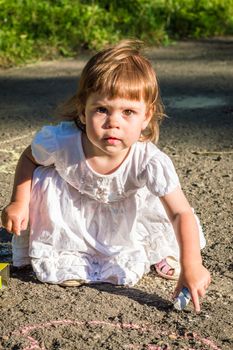 a little girl draws on asphalt in the Park in summer