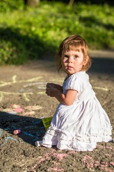 a little girl draws on asphalt in the Park in summer