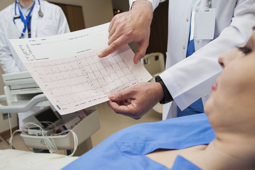 A young female patient is looking at a heartbeat diagram pointed by a doctor in hospital.