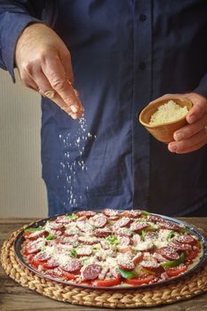 Man in a blue shirt sprinkle with cheese pizza from a ceramic sauser vertical