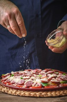 Man in a blue shirt sprinkle with cheese pizza from a sauser vertical