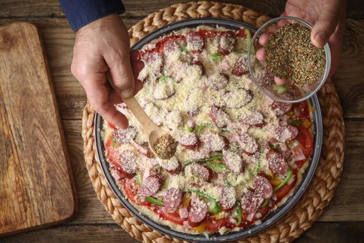 Man sprinkle with spice pizza from a glass sauser in a form horizontal