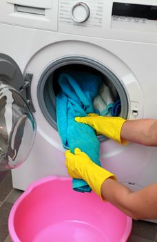 woman hands in gloves taking color clothes from washing machine
