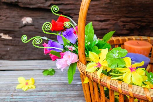 beautiful flowers plastic in a basket on brown wooden background