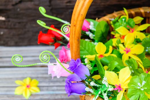 beautiful flowers plastic in a basket on brown wooden background