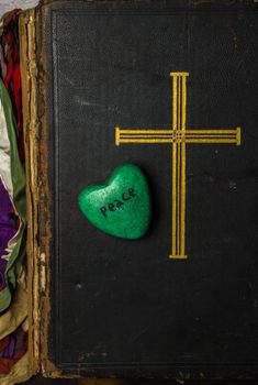 Catholic religion and peace concept represented by an old bible cover and a green - hope - heart.