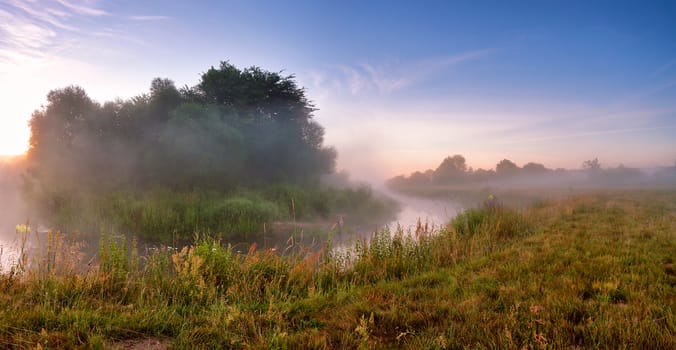 Summer misty sunrise on the river. Foggy river in the morning. Misty morning panorama.