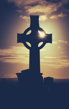 Vintage Style Image Of Sun Glinting Through A Celtic Cross Gravestone