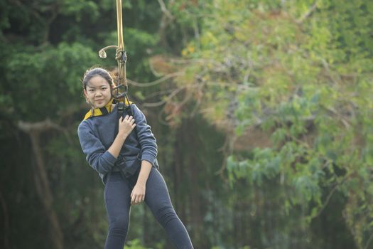 asian teen age  hanging on safety rope in outdoor adventure activity  with green blur background