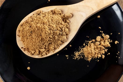 Brown cane sugar in a wooden spoon on the black background. Pure cane sugar for natural. no additives.