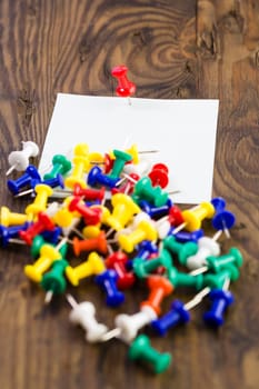 Thumbtack pins note to distressed wood surrounded by colored tacks