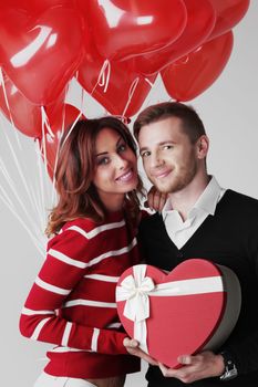 Happy embracing couple in love holding Valentines day gifts and bunch of heart shaped balloons