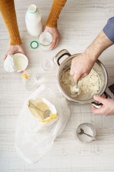 Man and woman makes the dough in the pan on the white table vertical