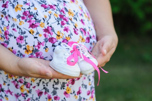 pregnant young mother holds white shoes child.