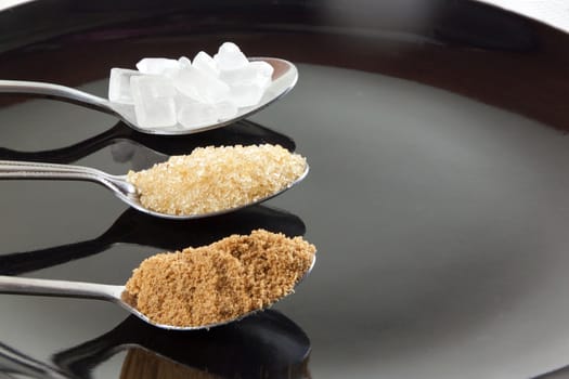 Brown cane sugar and granulated sugar and rock sugar in a metal spoon on the black background. Pure cane sugar for natural.