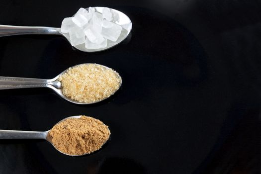 Brown cane sugar and granulated sugar and rock sugar in a metal spoon on the black background. Pure cane sugar for natural.