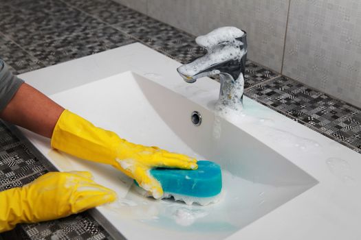 hands of woman in gloves who washes white sink in bathroom