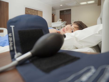 A young female patient looking to camera from a hospital bed through a blood pressure monitor.