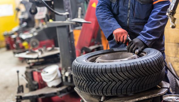 Professional auto mechanic replacing tire on wheel in car repair workshop.