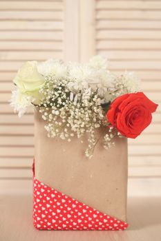 Beautiful bouquet of flowers in paper bag on wooden background, Valentines day gift concept