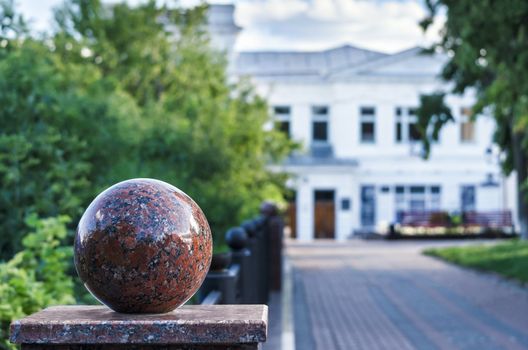 Granite balls in the city a fence in a shady alley. Selective focus, blurred building in the background.