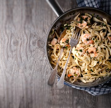 Tagliatelle with shrimps on the pan placed on a wooden surface