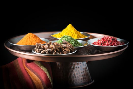 Five colorful spices on a copper presentation plate.