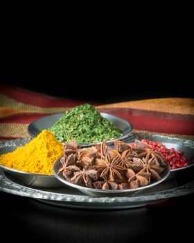 A selection of spices including star of anise, pink peppercorns, curry and parsley.