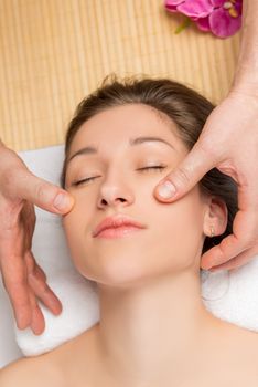 portrait of a relaxed girl and hands of a massage therapist on her face