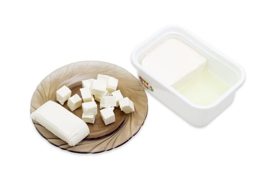 Container of feta cheese and sliced cheese on a saucer