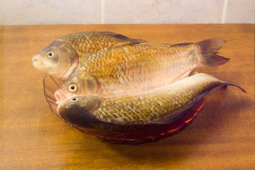 Three carps with peeled scales on red glass dish and prepared for cooking on a light background. Isolation.

