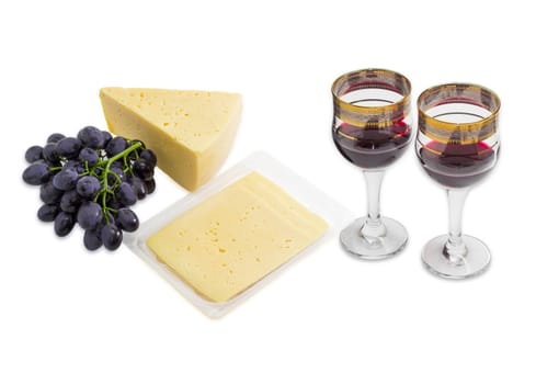 Two wine glasses with red wine, cluster of a blue grape, piece of cheese and several slices of cheese in plastic tray on a light background
