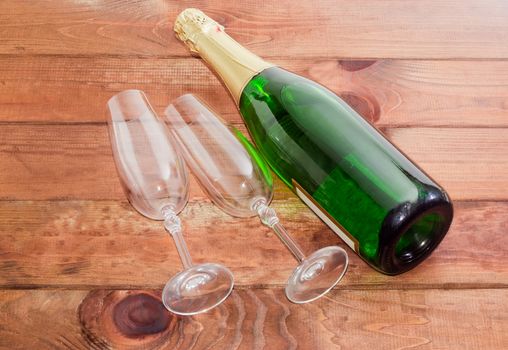 Two empty wine glasses and a bottle of sparkling wine on dark wooden surface
