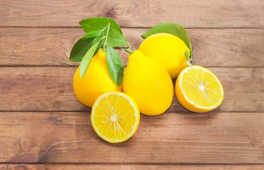 Several whole fresh yellow lemons with twigs and leaves and one lemon, cut in half on a dark wooden surface
