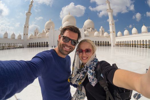 Tourist couple taking selfie in the courtyard of famous Sheikh Zayed Grand Mosque in Abu Dhabi, United Arab Emirates.
