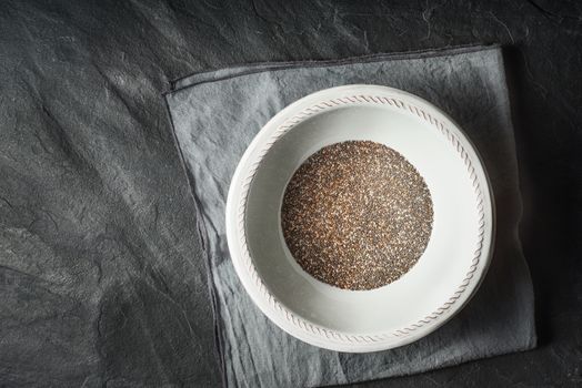 Chia seeds  in the white plate on the dark stone table top view