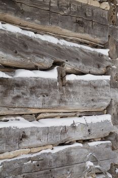 A festive winter background with weathered silvery grey horizontal sawn logs with snow in between.   Logs angle towards the corner of building.