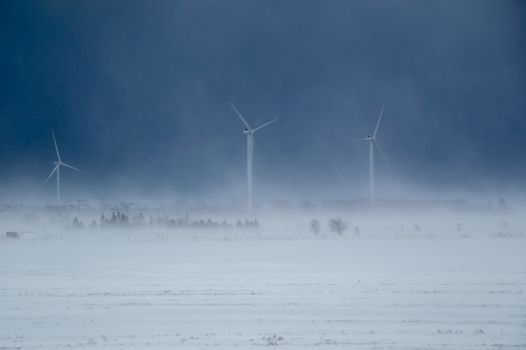 Image shows drifing snow blowing  to the height of the 3 windmills.  Green energy.