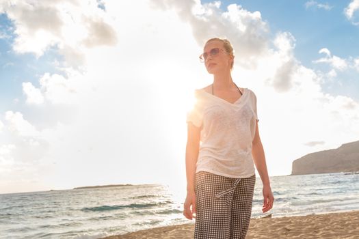 Relaxed woman enjoying sun, freedom and life an a beautiful sandy beach. Young lady feeling free, relaxed and happy. Vacations, freedom, happiness, enjoyment and well being.