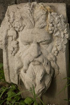 A cement stone green mans face in the leaves, spirit of the woods.