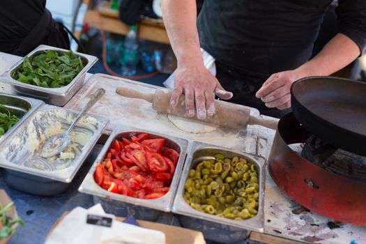 Chef making pita bread for falafel roll outdoor on street stall on Open kitchen international food festival event in Ljubljana, Slovenia. Street food ready to serve on a food stall.