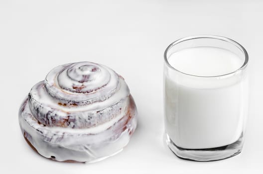 Bun with icing and a glass of milk on white background