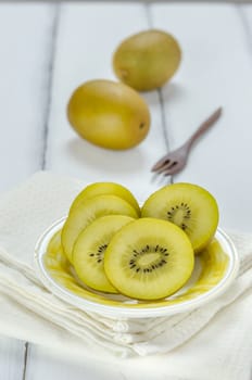 golden kiwi fruit and sliced on dish over white wooden background