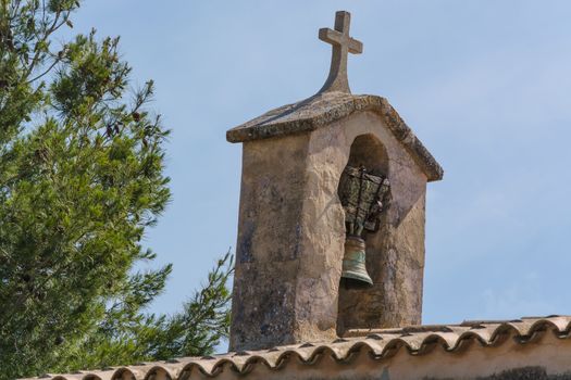 Church tower with bell in Spanish style against a blue sky.
