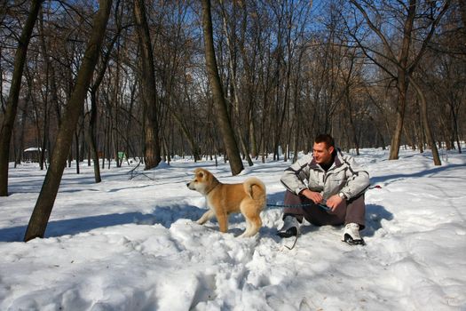 Young man enjoying on the snow  with its Akita Inu puppy