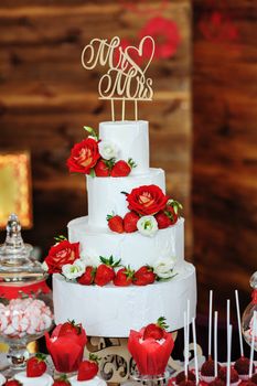 beautiful three-layered wedding cake decorated with red flowers.