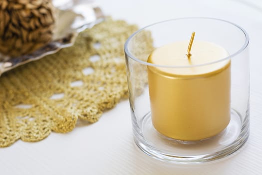 holiday golden candle in a glass over a white table
