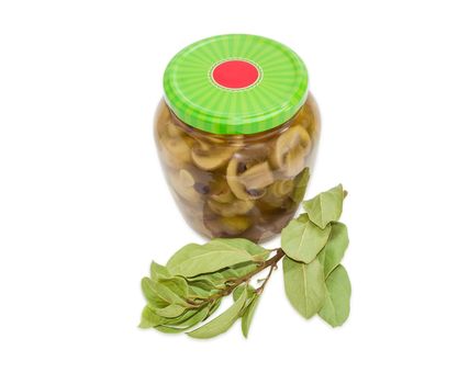 Pickled button mushrooms in glass jar with green screw cap and dried branch of a bay laurel on a light background
